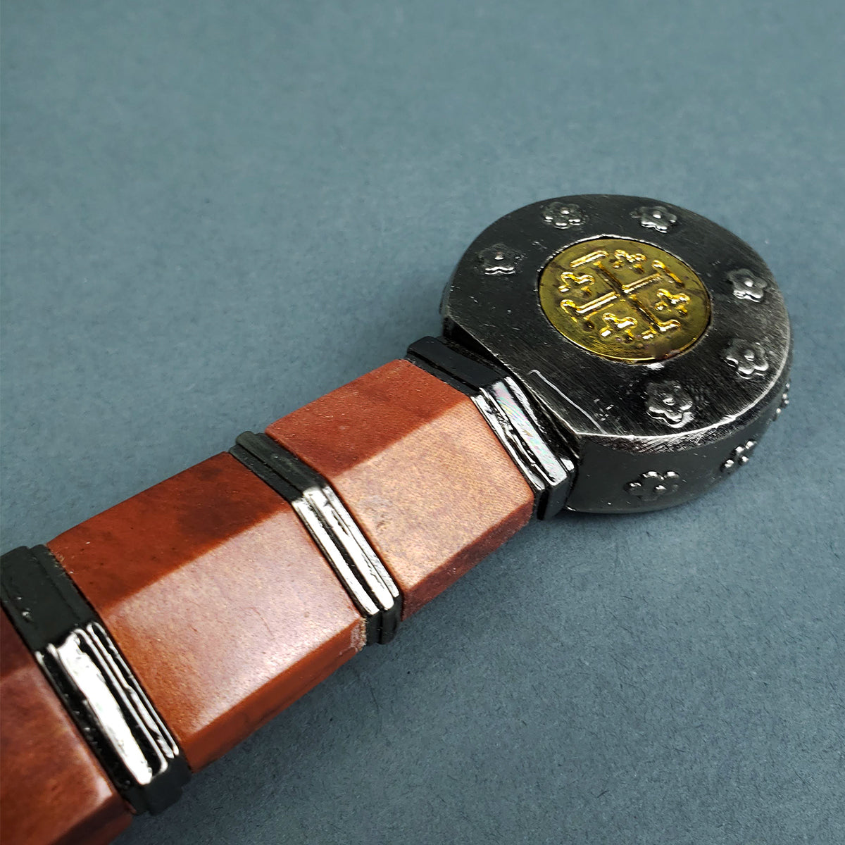 Close-up of Knights Templar short sword wooden handle with metal pommel featuring engraved cross design