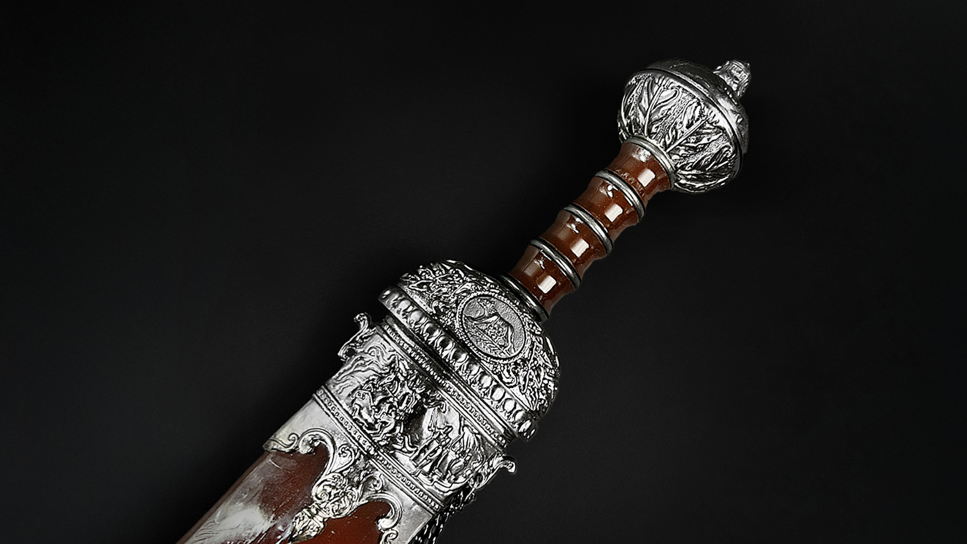 Roman and Viking swords for sale showing a Roman Gladius sword with detailed hilt and black leather scabbard on dark background